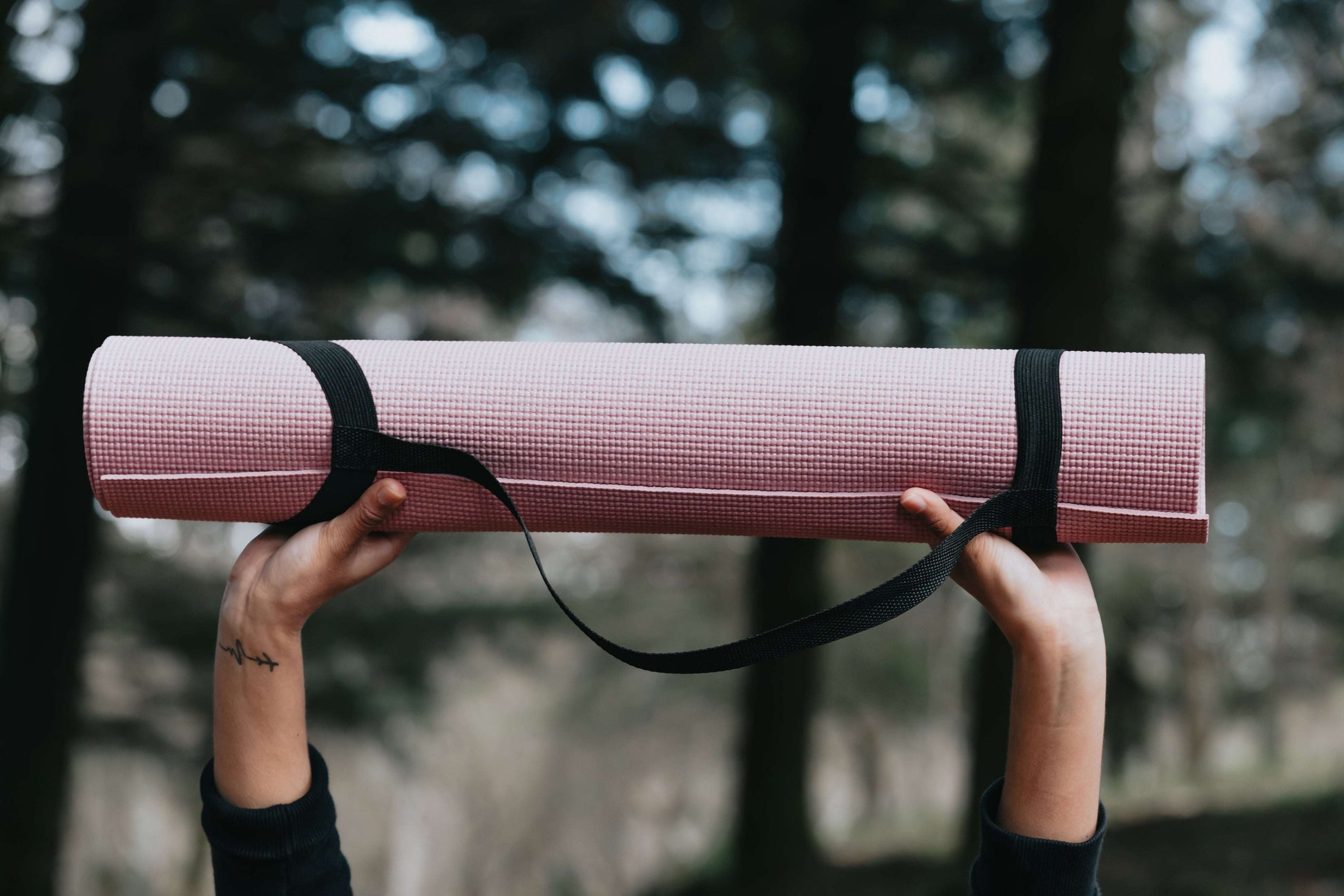 Lightweight pink yoga mat with a non-slip texture and black carrying strap held outdoors for an adventurous wellness session. [ShopZip]